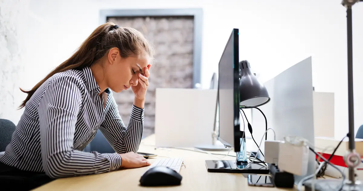 close-up photograph of a business owner rubbing their forehead in stress while looking at a chaotic inbox and spreadsheets, representing the inefficiency tax.